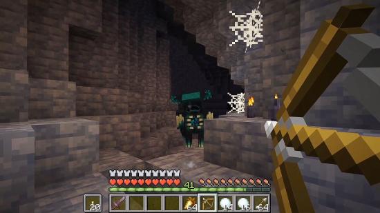 Minecraft Warden: Um guardião aparece em uma caverna, cercado por ardósia profunda e teias de aranha, enquanto o jogador prepara seu arco.