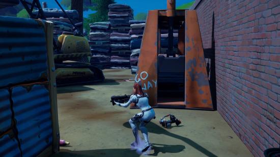 Player walking close to one of the car parts in the junkyard outside of Dirty Docks in Fortnite. There is a machine that says "Go Away" behind it.