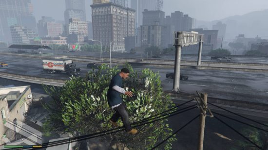 GTA 5 cheats - Franklin is jumping extremely high into the air, clearing the telephone cables and tree behind him. There is also a freeway and tall buildings behind him.