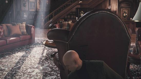 Agent 47 hiding behind a leather chair