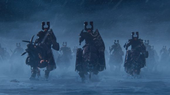 A group of charging Skullcrushers, heavy cavalry of Khorne wearing chunky red and brass armour, in Total War: Warhammer 3