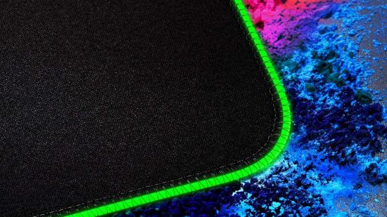 A close-up of a black mouse pad showing green RGB lighting around the edges