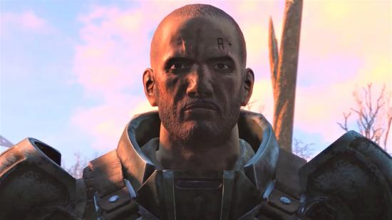 A cropped-haired man in chunky metal armour looks beyond the camera with a sunset behind