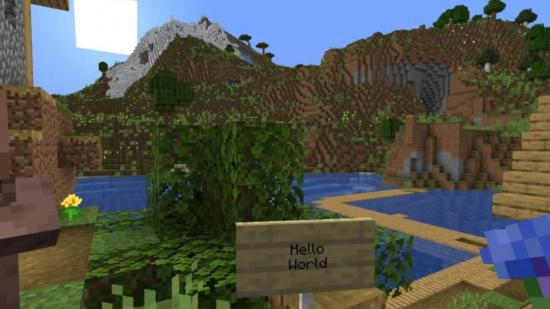 A Minecraft sign says 'hello world' in front of a river and mountain range