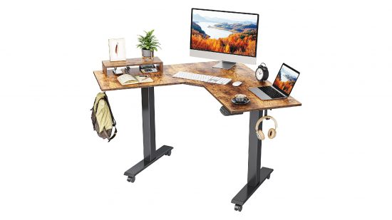 El mejor escritorio para estar de pie en una esquina es el Fezibo Dual Motor, con una mesa de madera más oscura y patas de marco negro, que se ve aquí con un monitor y una computadora portátil encima