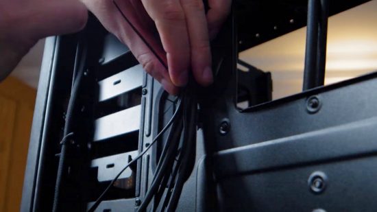 Cara Membangun PC Gaming: Seseorang mengikat kabel di bagian belakang PC gaming