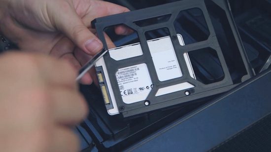 How to build a gaming PC: a hand screws the SATA SSD onto a bracket