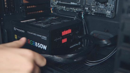 How to build a gaming PC: the modular power supply unit sits in the case as a hand plugs in cables