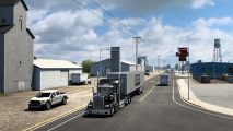 American Truck Simulator Montana release date: A black big rig pulling a 'NAMO' trailer pulls through a Montana town's warehouse area.