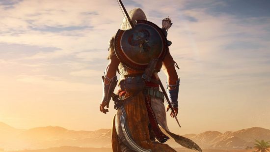 assassin's creed origins character walks through sand dunes in desert with a shield and spear as wind blows