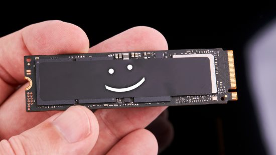 A person holds up an NVMe SSD with a smiley face in the centre