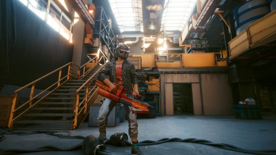 Cyberpunk 2077 mod garage: A male V wearing a padded motorcycle helmet holds a heavy machine gun painted with a flame design while standing in a cluttered warehouse lit by skylights above.