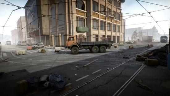Escape from Tarkov screenshots: A large orange flatbed utility truck parked in the street underneath tram lines in front of a tall downtown building