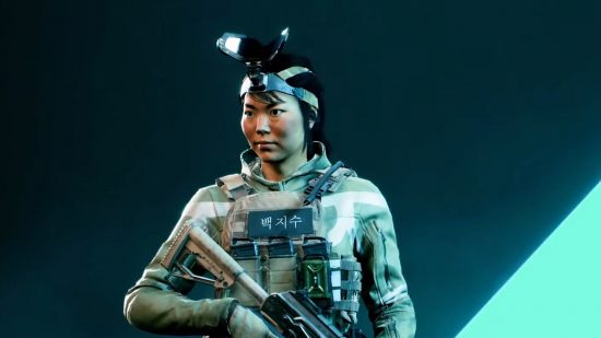 Battlefield 2042 update 2.0.1 - Ji-Soo Paik stands with body armour and a rifle held at the ready, her visor-style scanner flipped up over her head