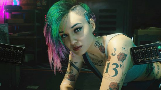 A woman with multi colored hair and several tattoos leans forward while facing the camera