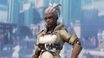 Overwatch 2 heroes: A woman of color wearing grey and white armor stands against the backdrop of a large city