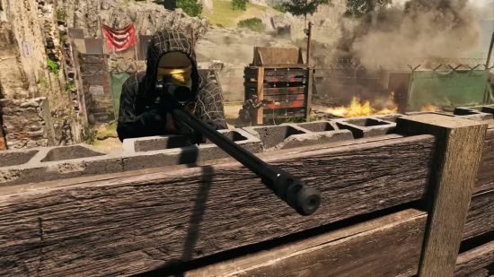 Mejores juegos multijugador: un francotirador con camuflaje completo tiene como objetivo disparar en Warzone 2. Otro jugador está disparando hacia un fuego detrás de un marco de escalada