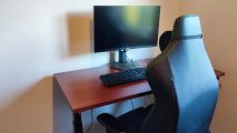 Flexispot E8 review - the standing desk has a red wood tabletop that holds a monitor, keyboard, and sits next to a Razer gaming chair