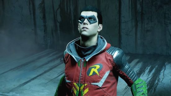 Gotham Knights cast: Robin is trapped in a chamber. He is looking around for an exit. His style is a red hoodie with the Robin logo on the chest.