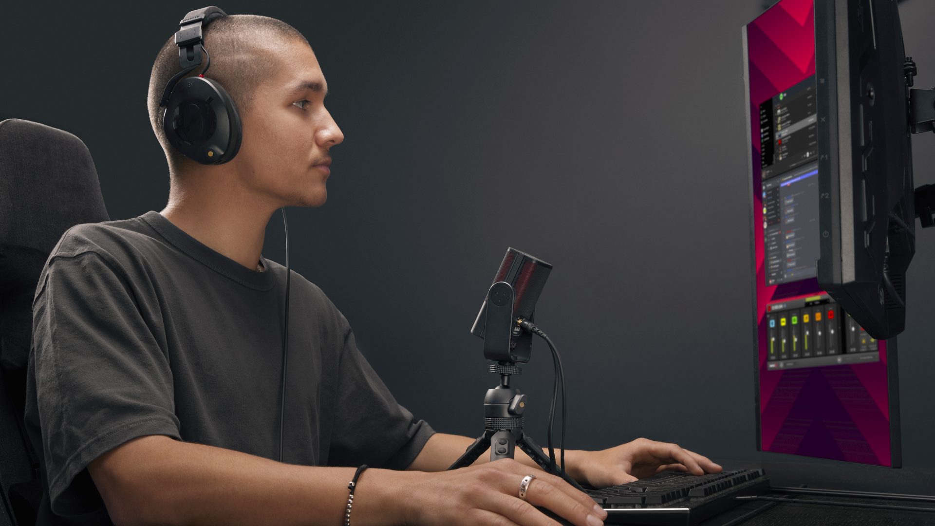 Mann mit Rode X-Mikrofon am Schreibtisch mit vertikalem Monitor und grauem Hintergrund