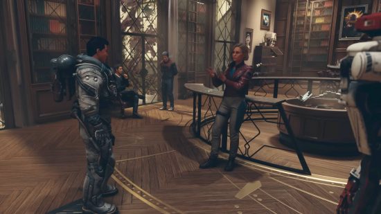 The player in a spacesuit has entered the Starfield Constellation headquarters inside a library with a display table in the center. He is talking to Sarah, who is wearing a maroon leather jacket, while other members talk to each other in the background.