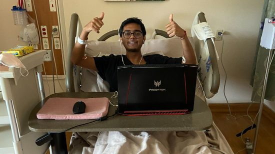 This Valorant player competed from a hospital bed and still won: a photo of Nishil smiling from their hospital bed, with a laptop and mouse in front of them, after playing Valorant