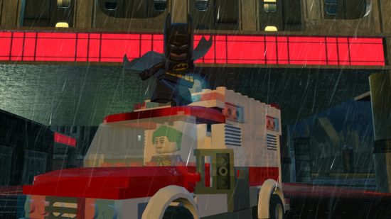 Best Batman games - Batman on top of an ambulance being driven by The Joker in LEGO Batman 2. It's passing under a bridge. 