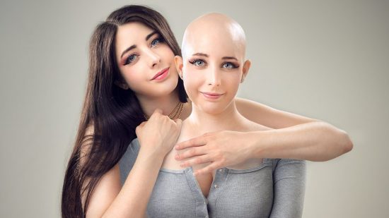 Cosplay with cancer: The story of Mikomi Hokina: A woman with long dark hair hugs a bald woman in a grey long sleeved jumper from behind