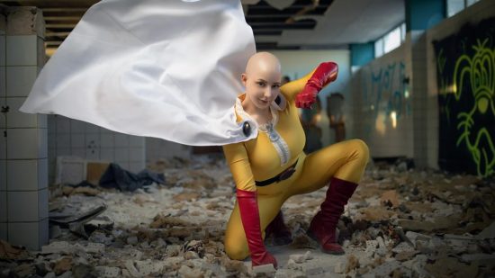 Una mujer calva con un traje de superhéroe amarillo con guantes rojos y una capa blanca que fluye golpea el suelo con una mano y lecturas para otro golpe