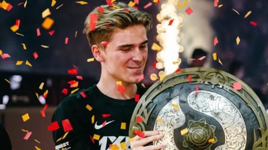 Dota 2 TI 2022 winners added to MOBA’s Aegis with awkward mistake: A blond man stands looking down at a huge shield-like trophy as confetti falls around him and a firework goes off in the background