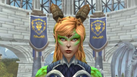 WoW Dragonflight Dracthyr is easier if you don't play as a dragon: A ginger woman with huge brown horns and neon green scales surrounding her eyes stands in Alliance stronghold Stormwind in a grey castle with two blue banners featuring a golden lion head