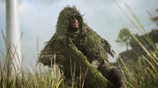 Call of Duty Warzone 2 patch proximity chat bug: A sniper in a green ghillie suit holds a rifle covered in camo netting while sitting in a grassy field near the pylon for a wind turbine