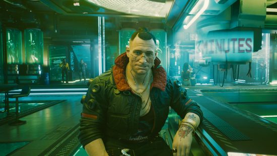 Cyberpunk 2077 lawsuit: Jackie Welles sits, smiling, at the Afterlife bar in Night City, his elbow on the bar and the scene lit in pale green-blue