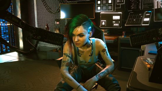 Cyberpunk 2077 saves Stadia: Judy Alvarez, a punky-looking young woman with a green undercut hairstyle, sits near her hacking desk, which has several high tech black-and-white computer monitors mounted to it