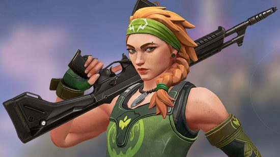 Valorant is adding team deathmatch, but it's no Call of Duty rip-off: A white woman with long ginger hair in a braid wearing a forest green headband and shirt hoists a huge rifle over her back shoulder looking into the camera