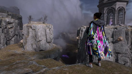 A black woman with her hair tied back in a bun stands in a rocky area wearing a garish cloak with cats on it and a black hood