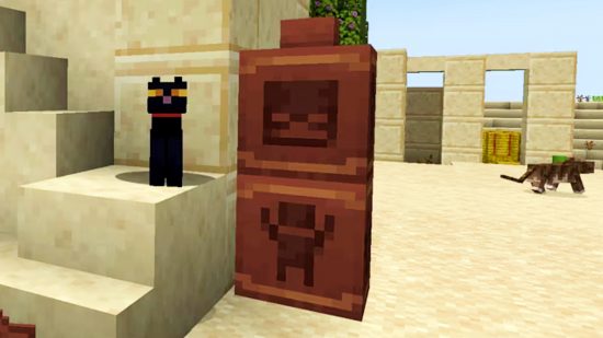 Minecraft update 1.20 - Archeology - two pots stacked atop one another by a desert temple. The top one has a painted design of a skeleton, while the bottom features a person with their arms raised. A black cat sits on a step next to them.