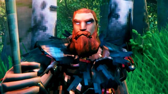 Valheim building update - a character with a hefty ginger beard standing in a forest, wearing a crow-feather cloak and holding up a torch