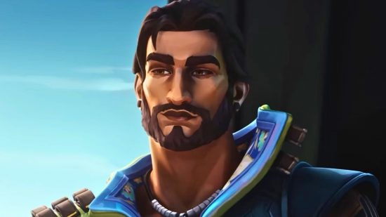 A handsome Indian man with a brown goatee and black ear piercings smirks into the camera on a sunny background