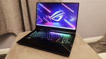 Asus ROG Strix Scar 17 review: A gaming laptop placed upon a beige stand, its RGB keyboard glowing brightly