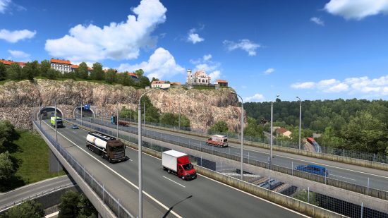 Beste pc -spellen - Euro Truck Simulator 2: een panoramisch uitzicht op een snelweg met een blauwe lucht, een paar wolken en sommige voertuigen die over de brug rijden