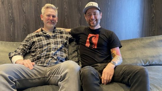 Darkest Dungeon 2 DLC will pay for devs to “keep making cool things”: two white men sit on a sofa smiling into the camera
