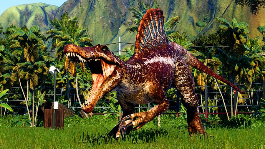 Jurassic World Evolution 2 - a dinosaur roars, surrounded by electric fences in a lush green environment