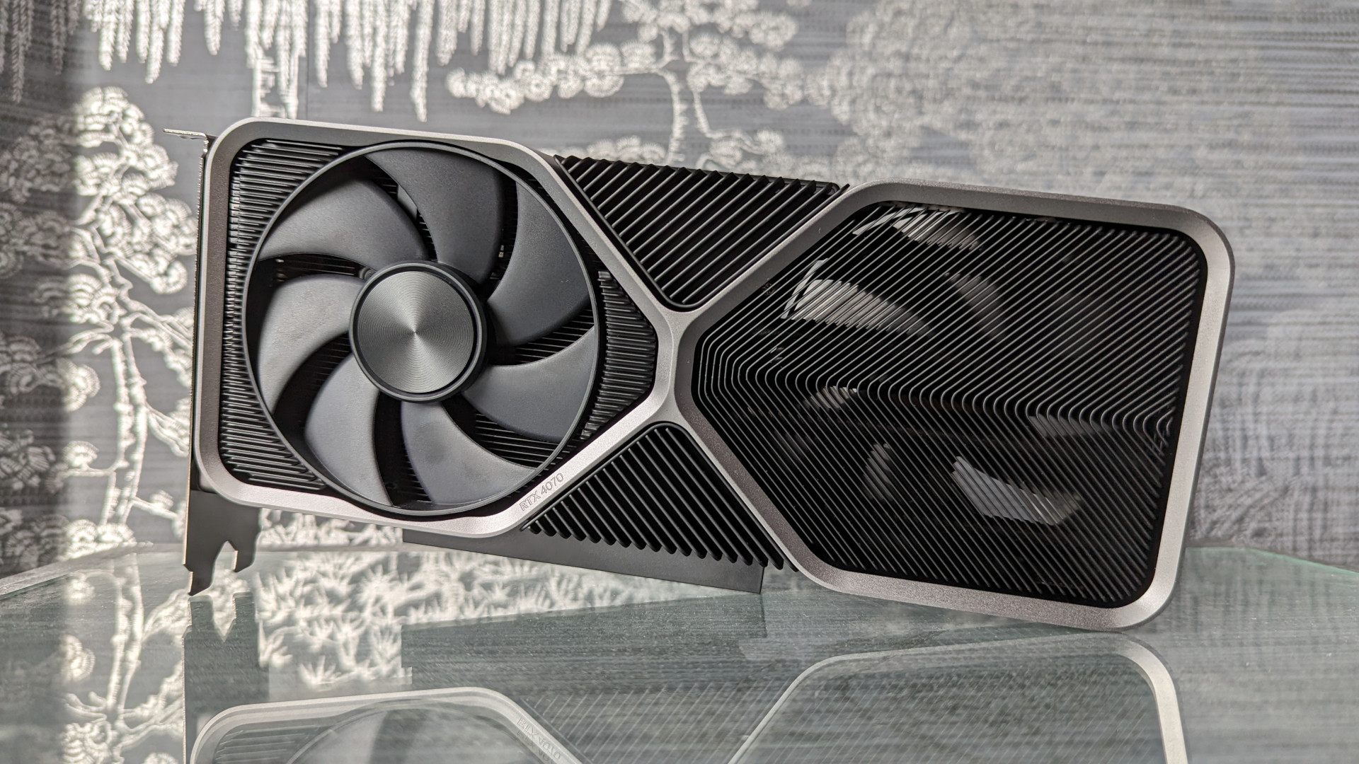 Nvidia Geforce RTX 4070 Đánh giá: Một card đồ họa phiên bản sáng lập phản ánh trên bề mặt kính, trên nền màu xám bạc
