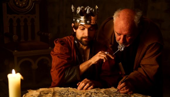 A bearded king with a shiny crown sits staring at a map under candlelight beside an old man