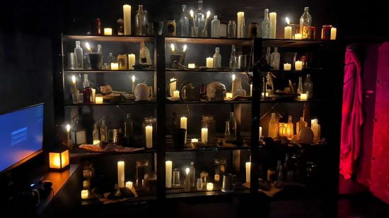 Diablo 4 chocolate shop - gaming setups in a darkened room next to a shelving display of candles, bottles, and jars.