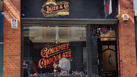 Diablo 4 chocolate shop - Lilith & Co, a storefront promising 'Goremet Chocolate' in gold and red lettering"