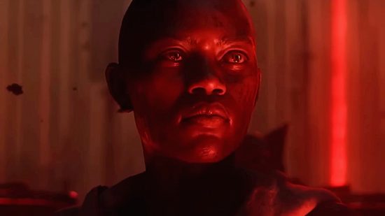 A bald woman in red lighting looks away from the camera, eyes wide