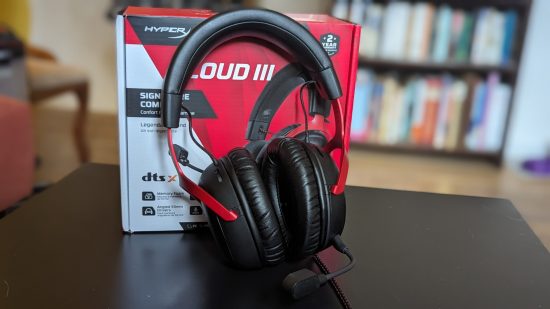 HyperX Cloud 3 review: a black and red headset is sat on a table next to its red and white box, with a bookcase in the background.