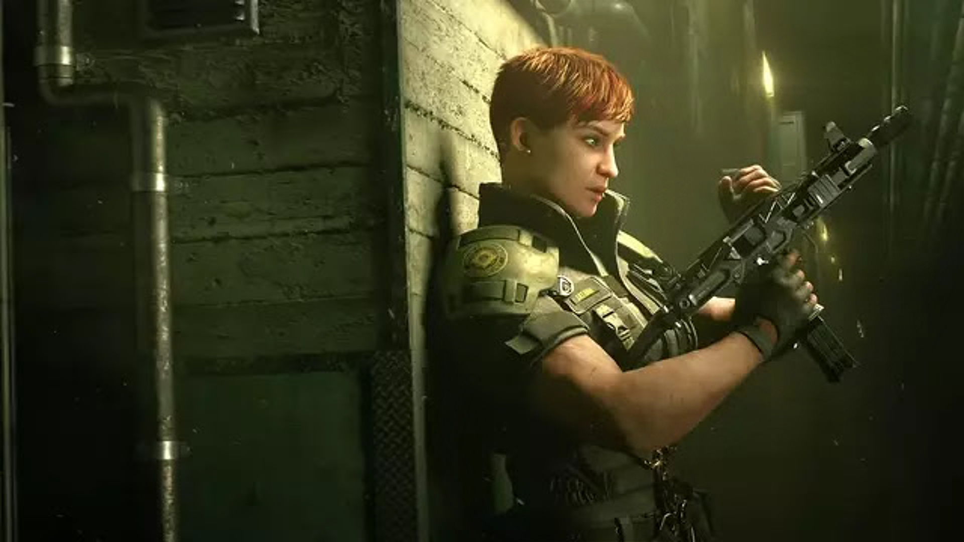 A short-haired woman wearing military gear and standing against a wall with gun in hand